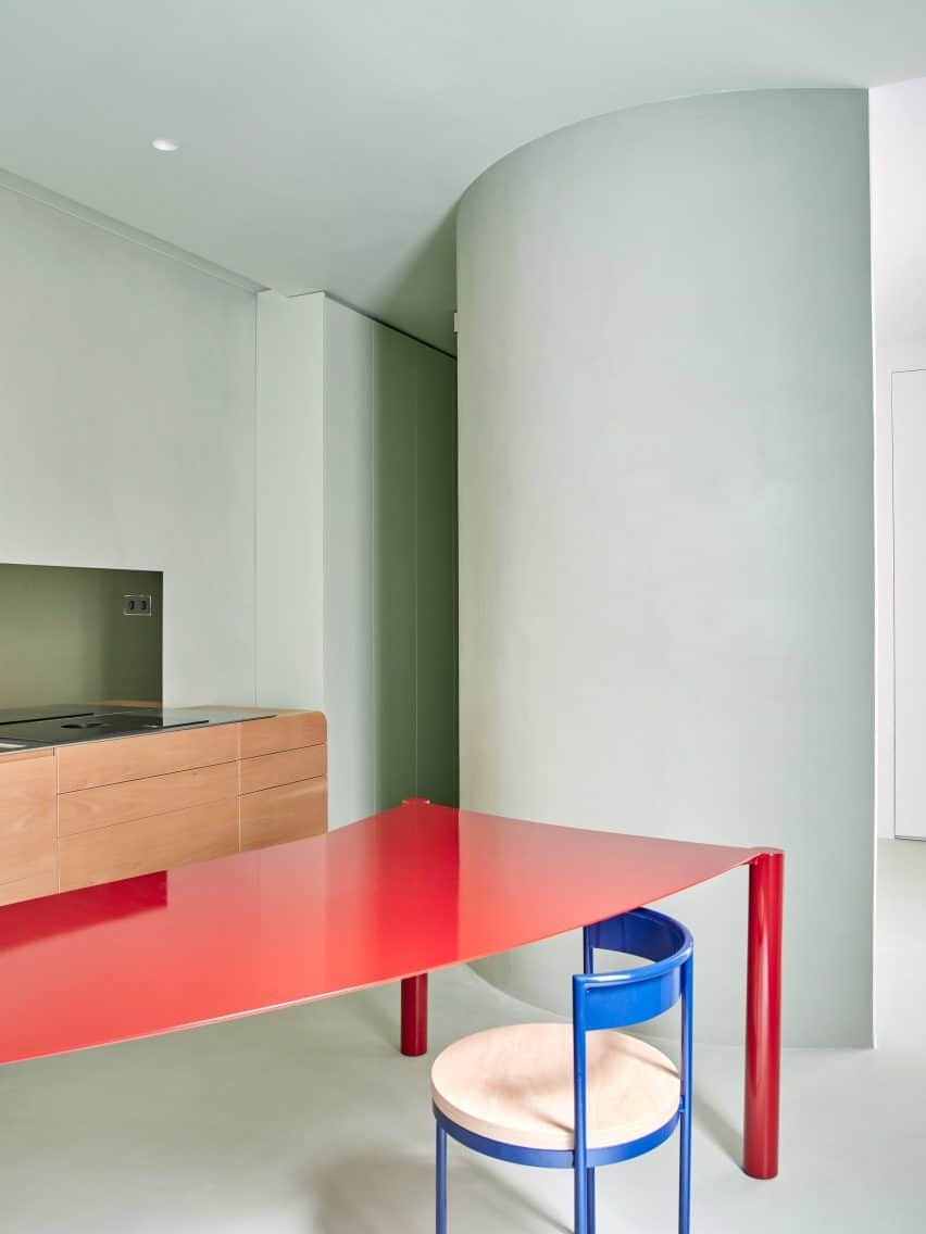 Image illustrating the Casa Milc kitchen, painted in pale sage green with a crimson dining table that complements the curved walls.