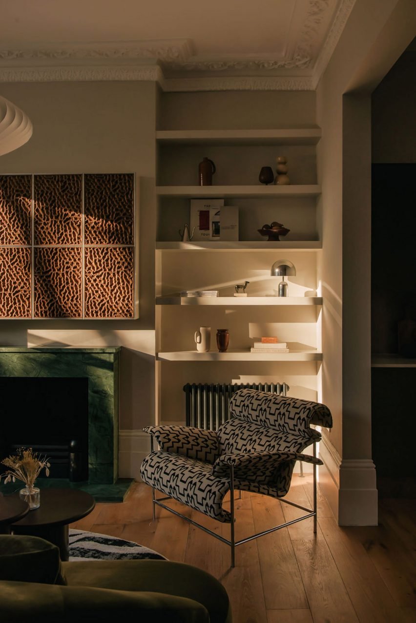 A London townhouse's living room with graphic fabric metal chairs and artistic decor above a green-marble fireplace.