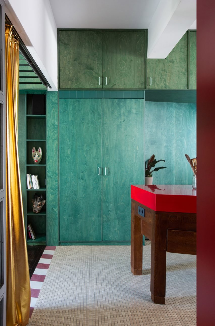 Image showing Trikoupi apartment with a vibrant stained plywood storage wall and oxblood-colored kitchen cabinets contrasting with a glossy red island.