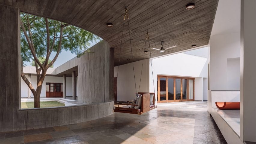 Covered walkway with swing seat looking out onto an open-air courtyard with trees