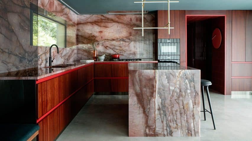 A red kitchen designed with quartzite featuring an island and splashback.