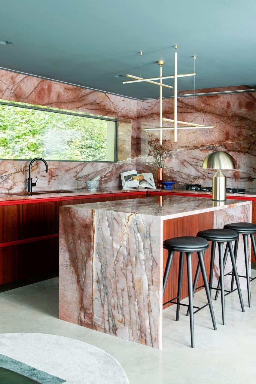 An open-plan kitchen defined by a red quartzite counter and ruby-toned timber cabinets.