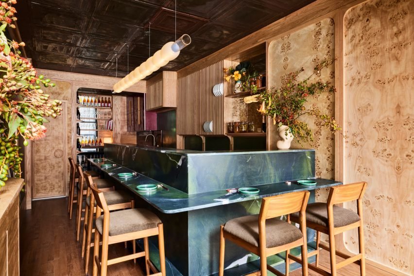 The interior of Bar Miller with dark blue-green counters and burl wood walls, highlighting its compact seating arrangement.