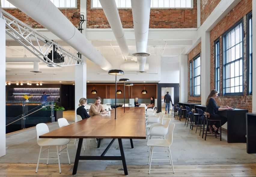 A large wooden communal table under clerestory windows bringing light into workspaces.