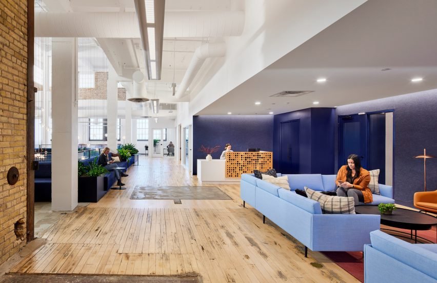 Blue lounge area to the right and open hallway to the left, showcasing exposed brick walls.