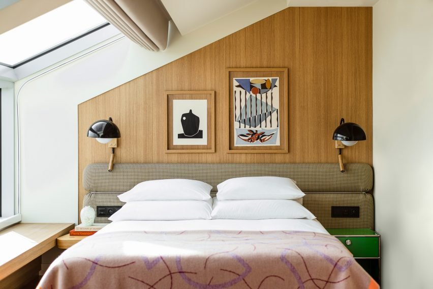 The hotel room features a soft upholstered headboard with integrated lighting and framed artwork.